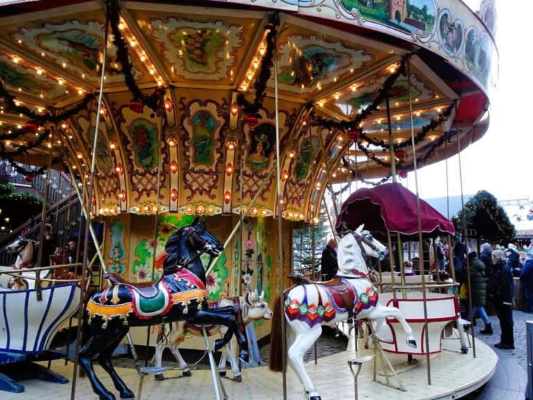 Un manège ancien illuminé, chevaux de bois peints au premier plan, sur le marché du Heumarkt
