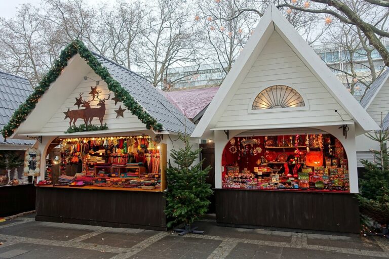 Deux chalets blancs décorés de branches de sapin, d’étoiles et de rennes en bois, sur un marché de Noël de Cologne