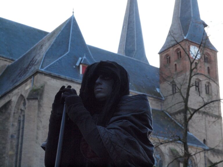 Personnage encapuchonné de noir, figure de fantôme du Dickens Festijn, devant les flèches de la Bergkerk de Deventer