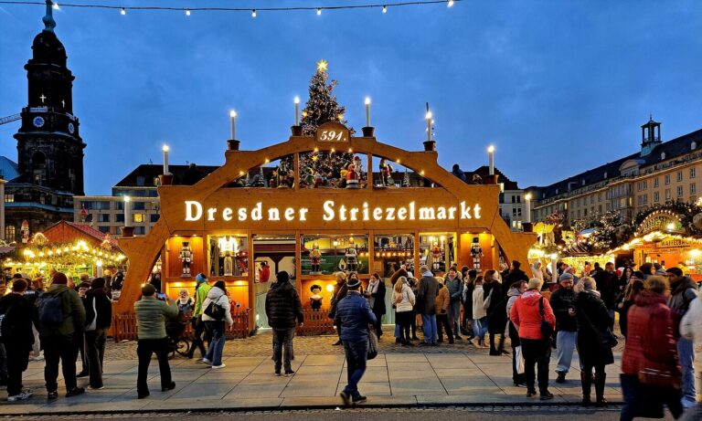 L’arche d’entrée en bois du Dresdner Striezelmarkt, surmontée de bougies et d’un sapin, à la tombée de la nuit