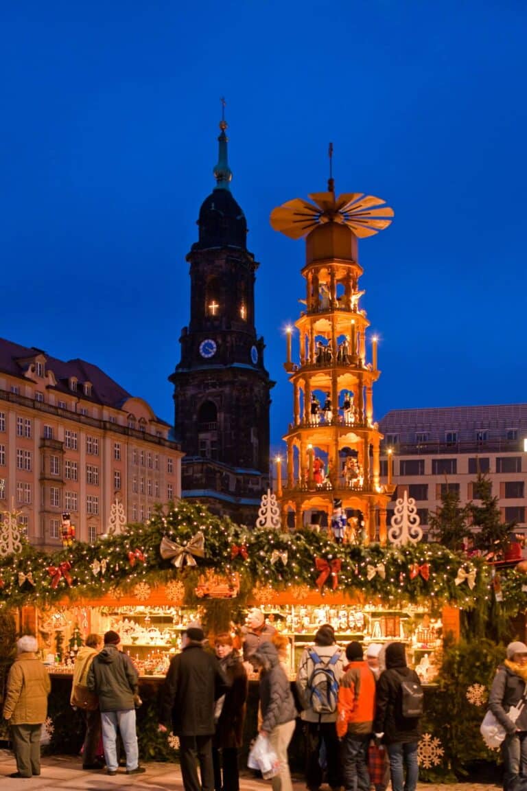 La grande pyramide de Noël illuminée à côté de la tour de la Kreuzkirche, au-dessus des chalets, sous un ciel bleu nuit