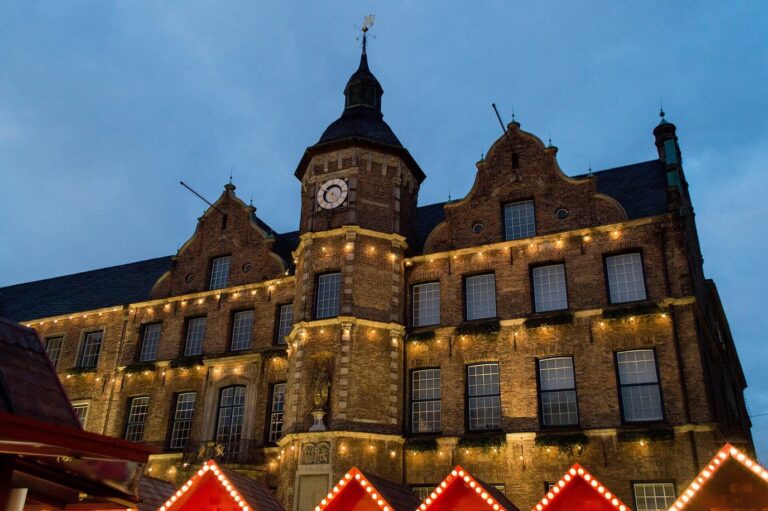 La façade Renaissance de l’hôtel de ville de Düsseldorf soulignée de guirlandes, au-dessus des toits rouges des chalets, le soir