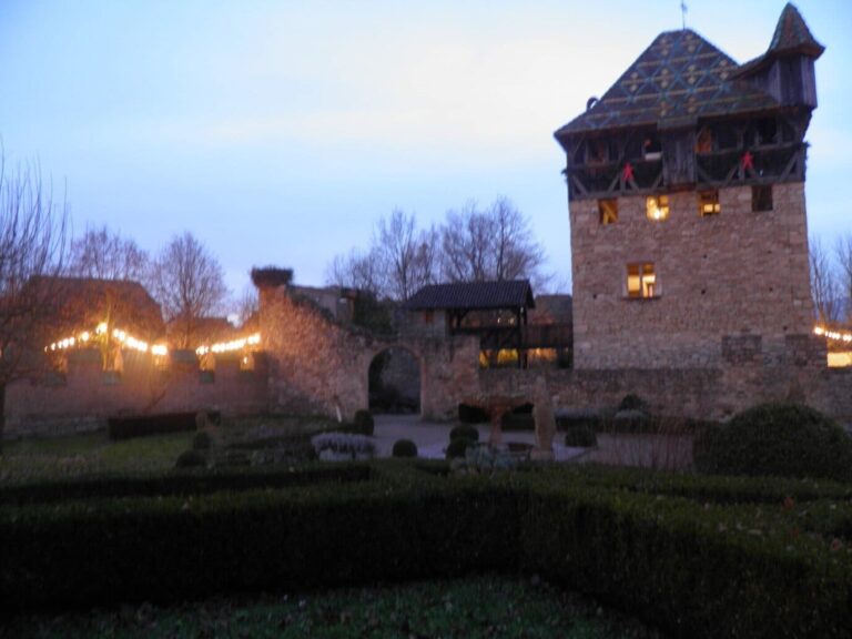 La tour forte et les bâtiments du village reliés par des guirlandes lumineuses, au crépuscule