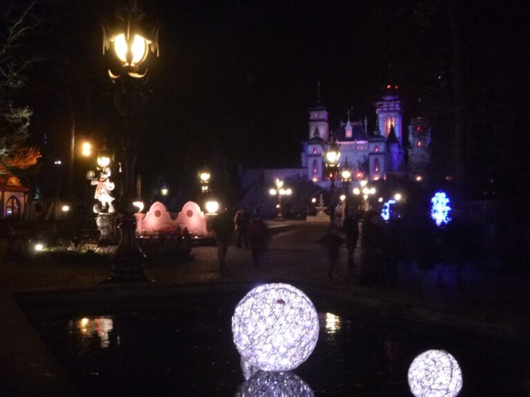 Allée du parc Efteling la nuit, avec lampadaires, boules lumineuses posées près de l’eau et palais illuminé en arrière-plan