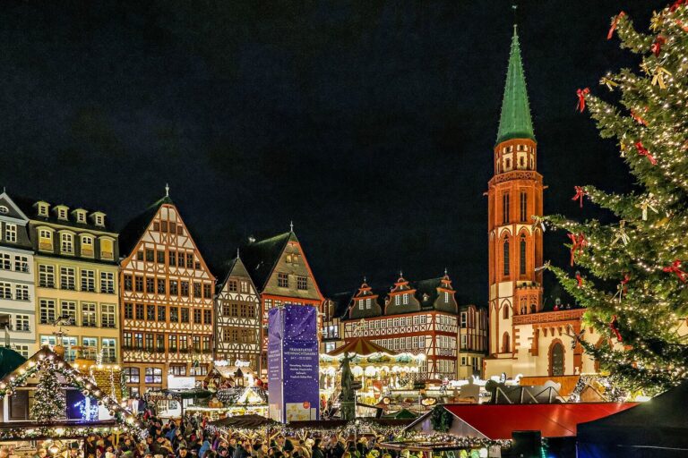 Chalets illuminés du marché de Noël sur le Römerberg, maisons à colombages et clocher de la vieille église Saint-Nicolas, avec un sapin décoré au premier plan, la nuit