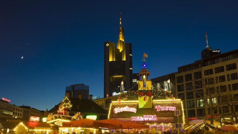 Chalets illuminés du marché de Noël au pied de la Commerzbank Tower et des immeubles du centre de Francfort, à la tombée de la nuit