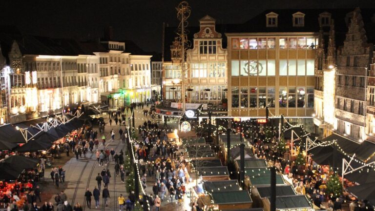 Vue plongeante sur les allées de chalets illuminés du marché de Noël de Gand, la nuit, bordées de façades à pignons