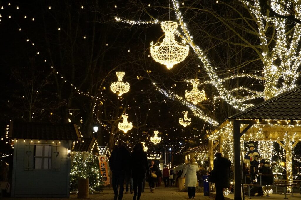Lustres lumineux suspendus dans les arbres au-dessus des chalets du marché de Noël de la promenade des Bastions, la nuit