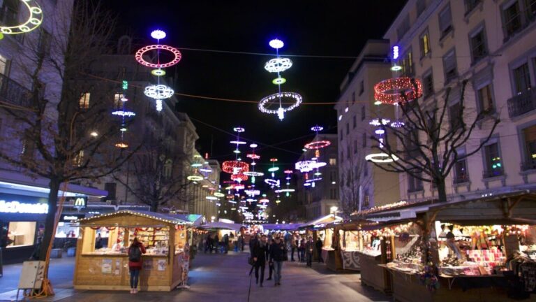 Chalets de Noël alignés dans une rue piétonne du centre de Genève, sous des anneaux lumineux colorés