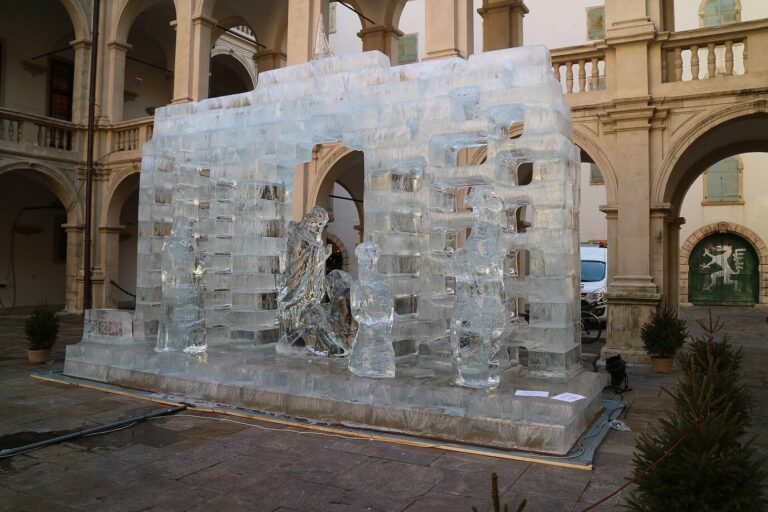 Crèche de glace aux personnages translucides dressée dans la cour à arcades du Landhaus de Graz, entourée de petits sapins