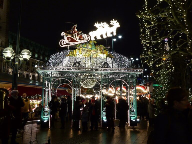 Le pavillon d’entrée illuminé du marché de Noël du Rathausmarkt, surmonté d’un traîneau et de rennes lumineux, la nuit