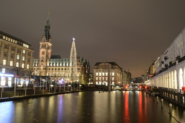 L’hôtel de ville et un grand sapin lumineux se reflétant dans le canal de l’Alster, le long des arcades de l’Alsterarkaden, la nuit