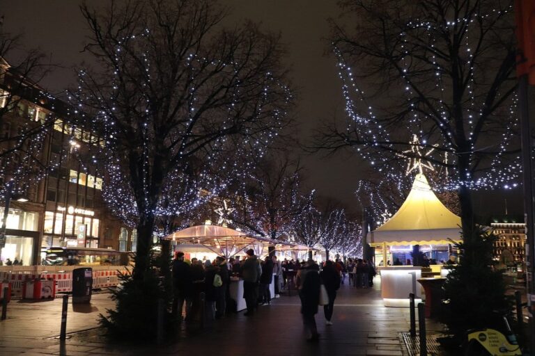 Les arbres du Jungfernstieg constellés de petites lumières au-dessus des stands blancs du marché de Noël, le soir