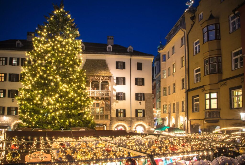 Le grand sapin illuminé du marché de Noël de la vieille ville d’Innsbruck devant le balcon du Petit Toit d’or et les façades anciennes, à l’heure bleue