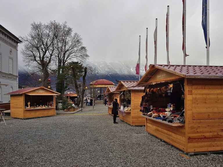 Chalets en bois du marché de Noël du Bergisel, sur une esplanade gravillonnée, avec les montagnes dans les nuages