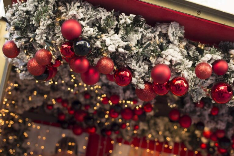 Boules rouges et branches enneigées décorant le toit d’un chalet, devant les guirlandes lumineuses du marché de Noël d’Innsbruck