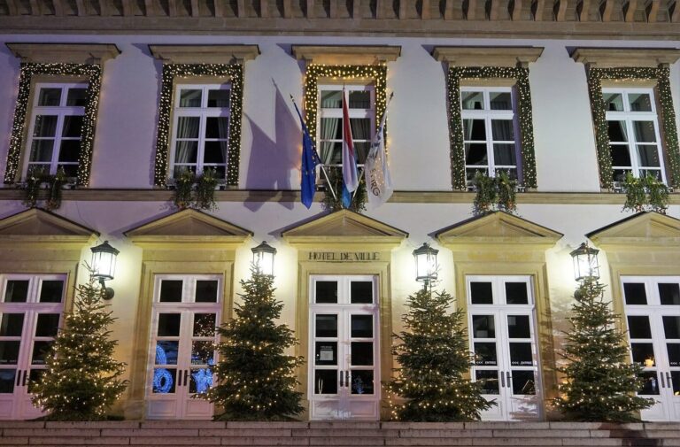 Façade de l’hôtel de ville de Luxembourg, place Guillaume-II, éclairée et bordée de sapins de Noël