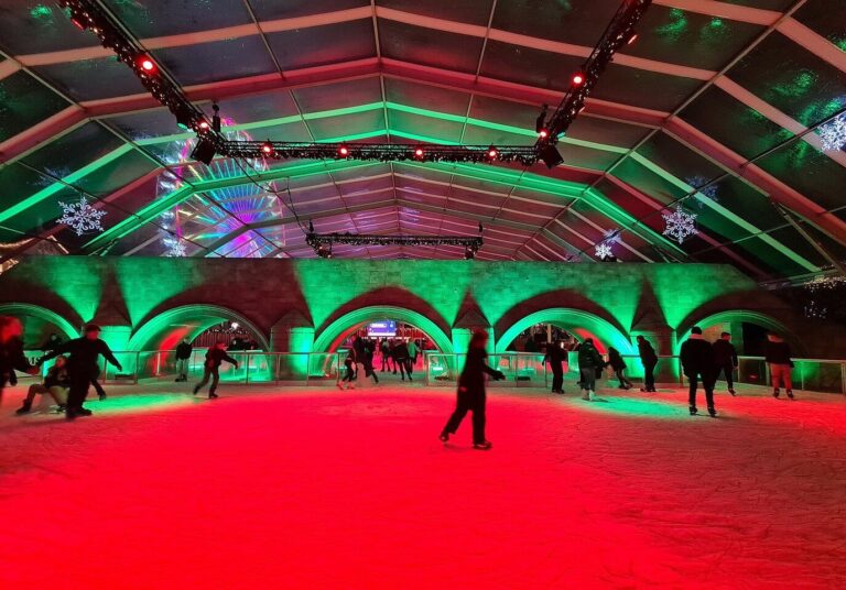 Patinoire couverte de Magisch Maastricht baignée de lumières rouges et vertes, sous une structure aux arches illuminées