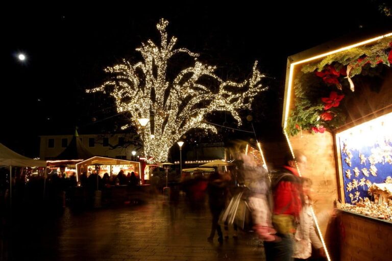 Grand arbre couvert de lumières au-dessus des chalets du marché de Noël de Merano, la nuit