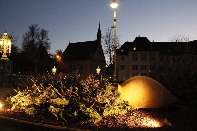 Décor de branchages éclairé et réverbères au crépuscule à Merano, avec la silhouette d’une église gothique en arrière-plan