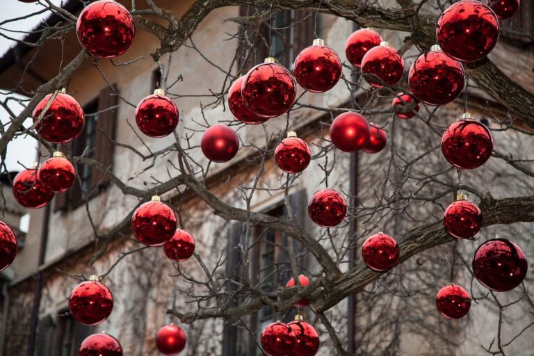 Boules de Noël rouges suspendues aux branches nues d’un arbre devant une façade ancienne de Merano