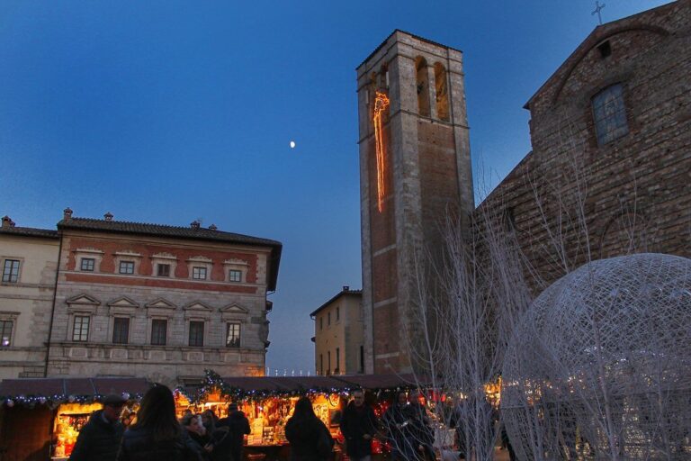 Le clocher de la cathédrale éclairé au crépuscule au-dessus des chalets lumineux du marché de Noël, avec une sphère décorative et la lune