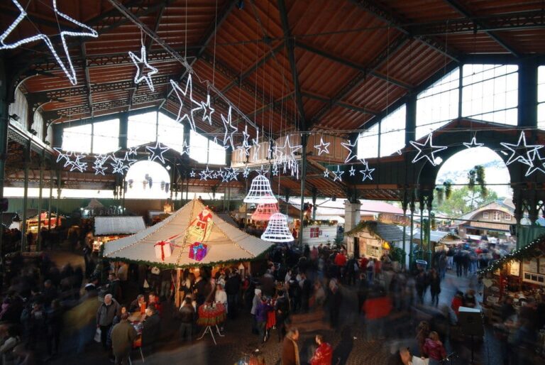 Chalets et stands sous la charpente du marché couvert de Montreux, décorée d’étoiles et de cloches lumineuses