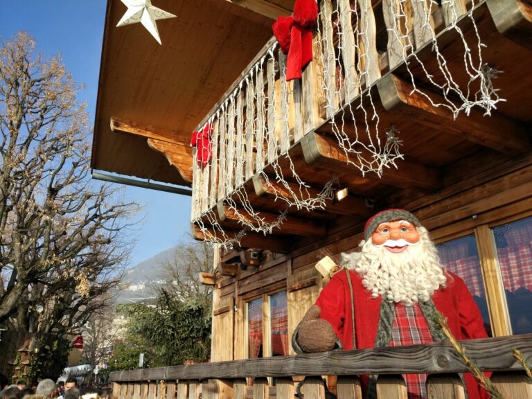 Figurine de Père Noël au balcon d’un chalet en bois décoré de guirlandes, sous un ciel bleu d’hiver à Montreux