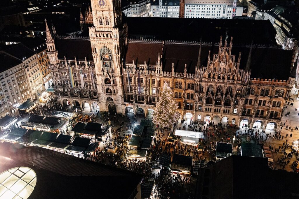 Le marché de Noël de la Marienplatz vu d’en haut, la nuit : rangées de chalets éclairés, grand sapin illuminé et façade néogothique du Nouvel Hôtel de Ville de Munich