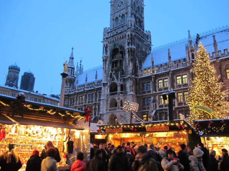 Chalets illuminés et sapin du marché de Noël devant le Nouvel Hôtel de Ville de Munich, avec les tours de la Frauenkirche, au crépuscule par temps de neige