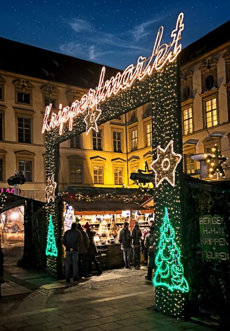 Arche lumineuse d’entrée du Kripperlmarkt, le marché aux crèches de Munich, avec ses sapins lumineux verts et ses étals, à la tombée de la nuit