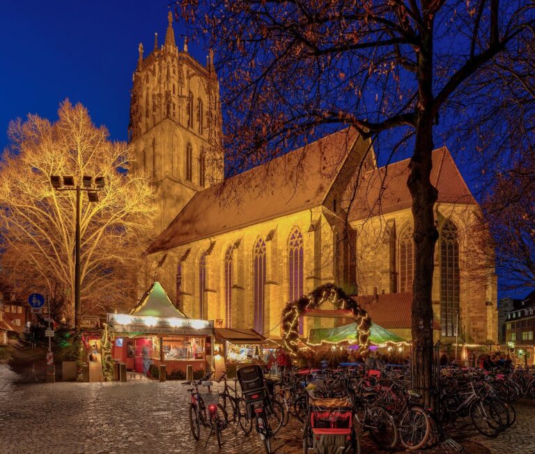 L’église Liebfrauen-Überwasser éclairée au-dessus des chalets du Giebelhüüskesmarkt et des arbres illuminés, à l’heure bleue