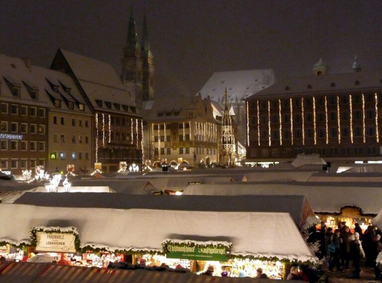 Le Hauptmarkt de nuit, chalets saupoudrés de neige et façades illuminées, avec les tours de l’église Saint-Sébald au fond