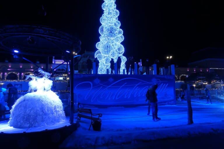 La patinoire éclairée en bleu, avec un sapin lumineux et une sculpture en forme de robe blanche, la nuit