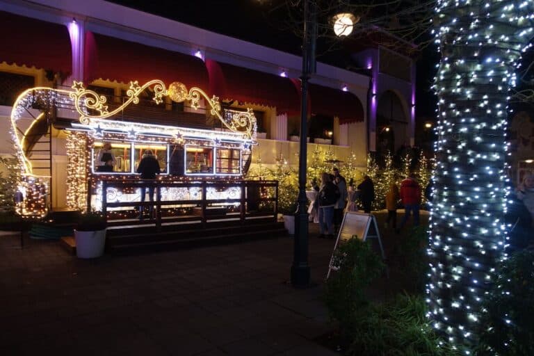 Un kiosque gourmand décoré de guirlandes lumineuses et d’étoiles, à côté d’un tronc d’arbre habillé de lumières blanches
