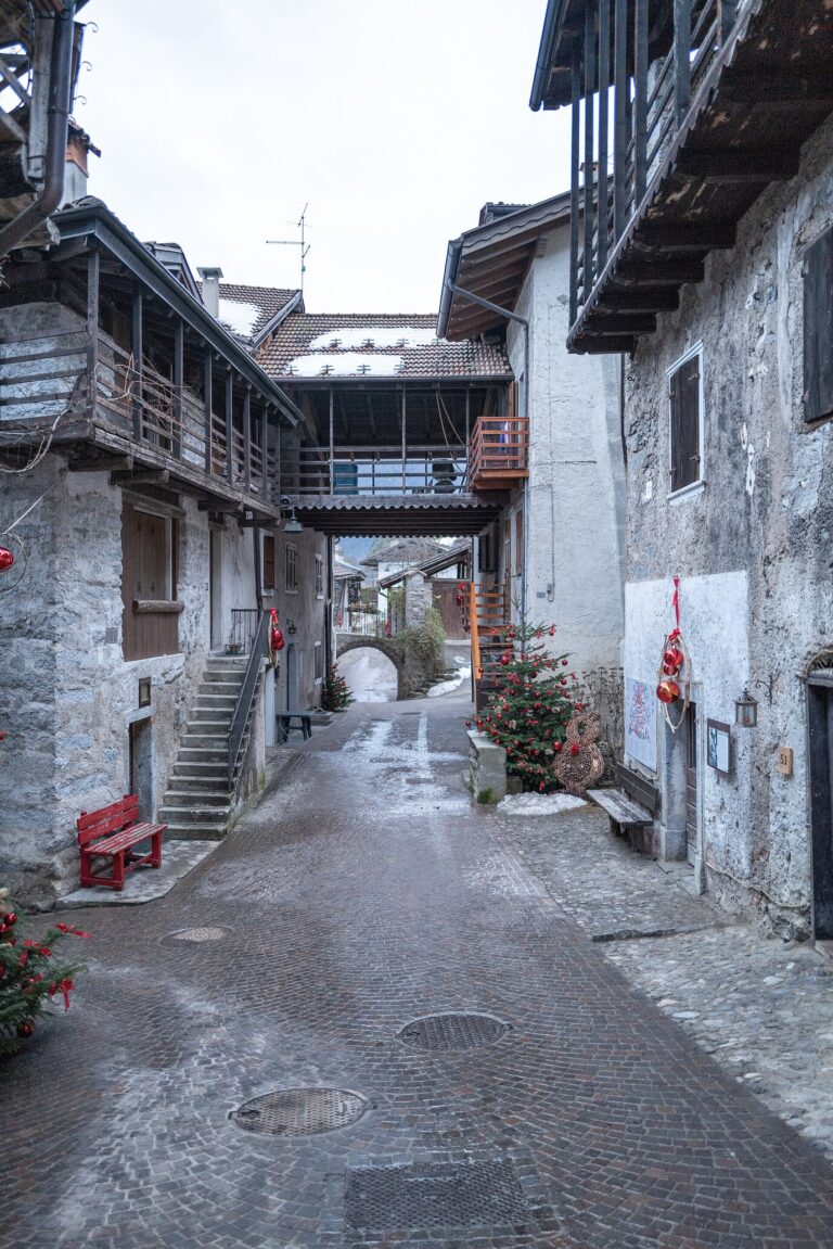 Ruelle pavée de Rango sous une passerelle couverte, un sapin décoré et un banc rouge le long des maisons de pierre