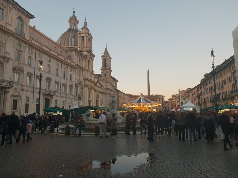 La piazza Navona au crépuscule pendant le marché de Noël : promeneurs, stands, manège illuminé, façade de Sant’Agnese in Agone et obélisque