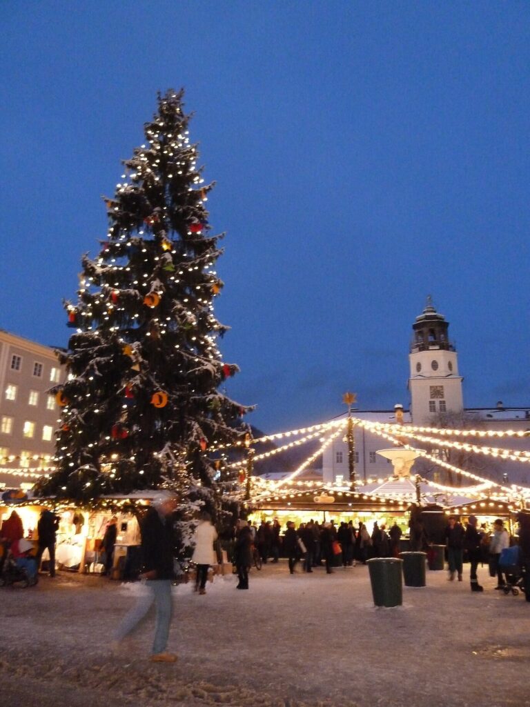 Grand sapin illuminé et chalets du marché de Noël à l’heure bleue, avec la tour du carillon de la Residenz de Salzbourg
