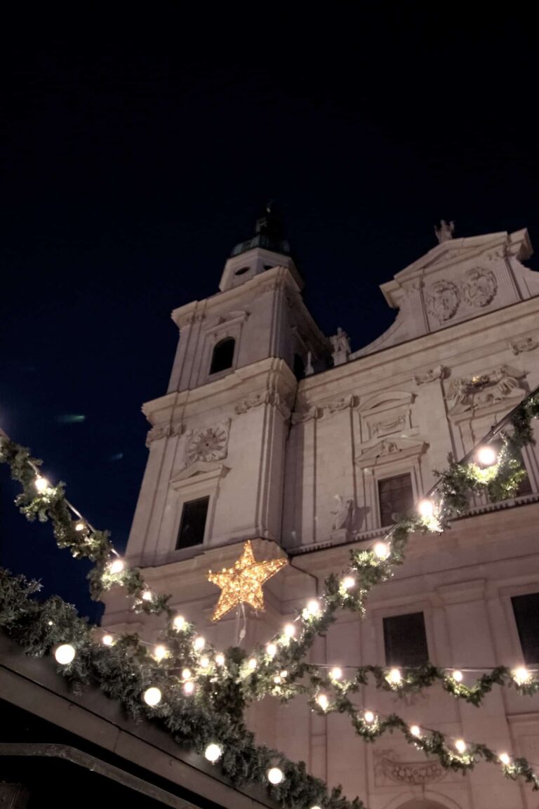 Guirlandes de sapin lumineuses et étoile dorée devant la façade blanche de la cathédrale de Salzbourg, la nuit