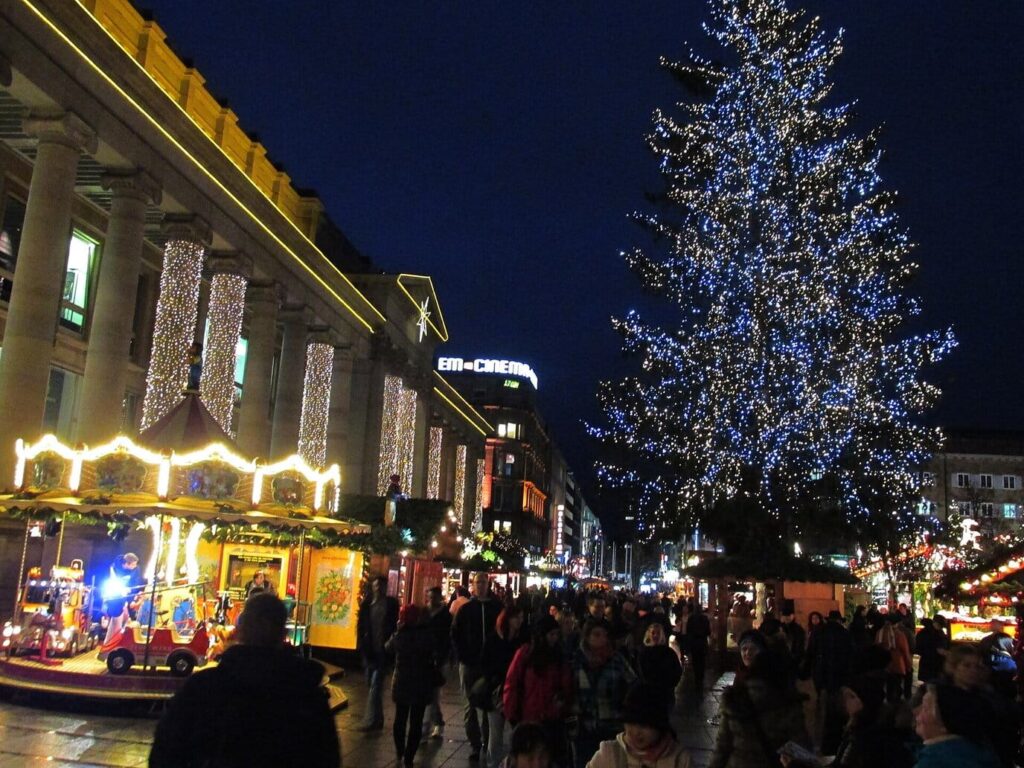 Le grand sapin aux lumières bleutées et un manège illuminé devant la colonnade du Königsbau, sur la Schlossplatz de Stuttgart, la nuit