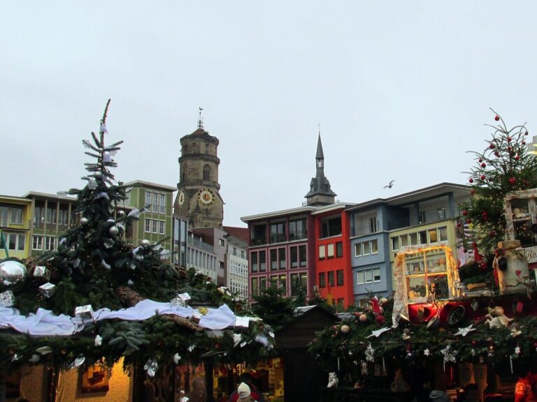 Toits de chalets garnis de sapins et de neige décorative sur la Marktplatz de Stuttgart, devant les façades colorées et la tour de la Stiftskirche
