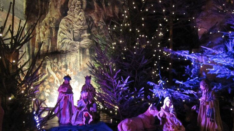 Scène de la Nativité éclairée de violet parmi des sapins couverts de petites lumières, dans la Gemeentegrot