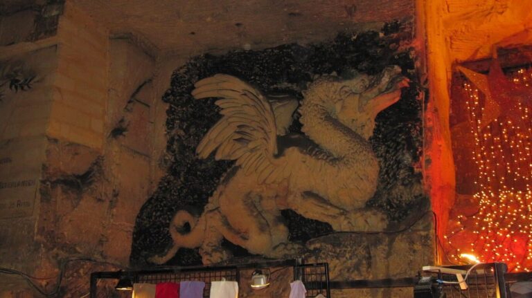 Sculpture d’un dragon ailé taillée dans la paroi de marne de la Gemeentegrot, à côté d’un rideau de lumières