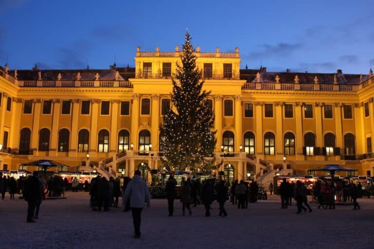 Le château de Schönbrunn éclairé à la tombée du jour, avec son grand sapin et les chalets du marché de Noël dans la cour d’honneur