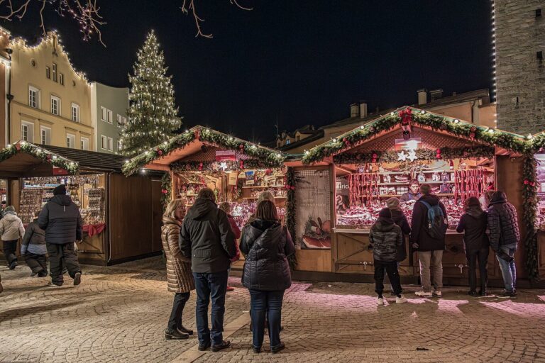 Visiteurs de dos devant les chalets décorés du marché de Noël, sapin éclairé et tour en arrière-plan