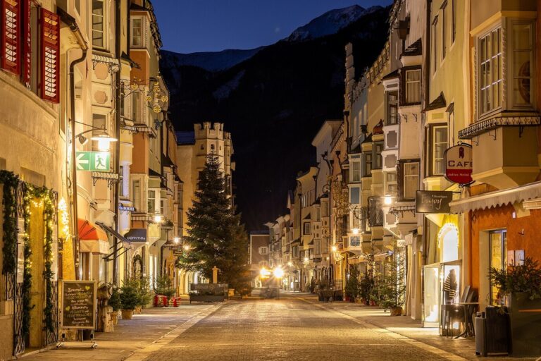 Rue de la ville nouvelle de Vipiteno illuminée pour Noël, un sapin au milieu et les montagnes au fond