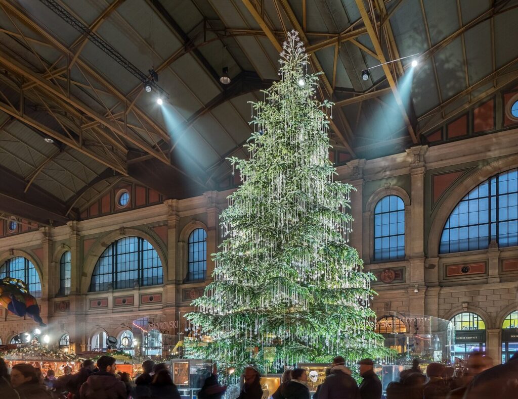 Sapin de quinze mètres couvert de cristaux au milieu des chalets du Christkindlimarkt, dans le grand hall de la gare centrale de Zurich