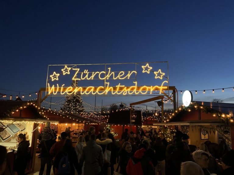 Enseigne lumineuse « Zürcher Wienachtsdorf » au-dessus des chalets du village de Noël du Sechseläutenplatz, à la nuit tombante