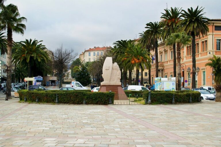 Le bas de la place Foch à Ajaccio, bordé de palmiers et de l’hôtel de ville rose, avec un sapin de Noël décoré et la statue de Napoléon au fond, en janvier