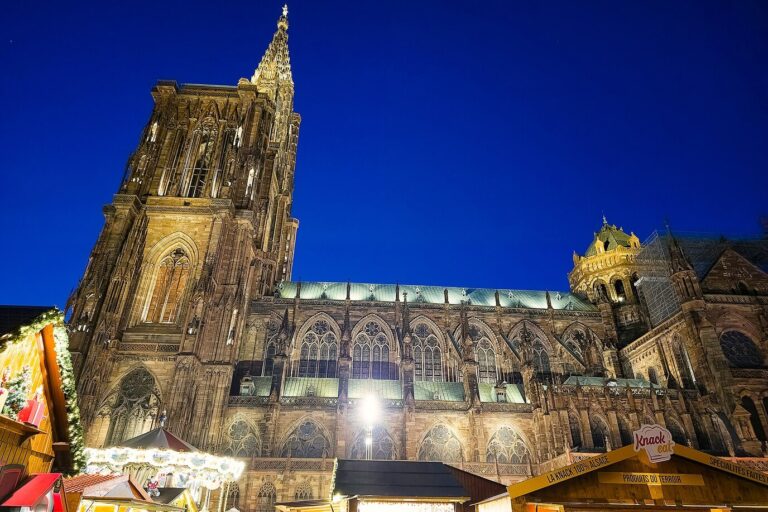 La cathédrale de Strasbourg illuminée à la nuit tombée, avec les chalets du marché de Noël à son pied